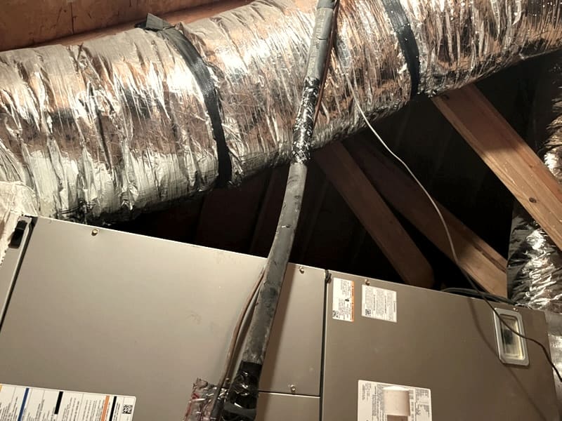 Two air handler cabinets in an attic with a duct trunk running over them.