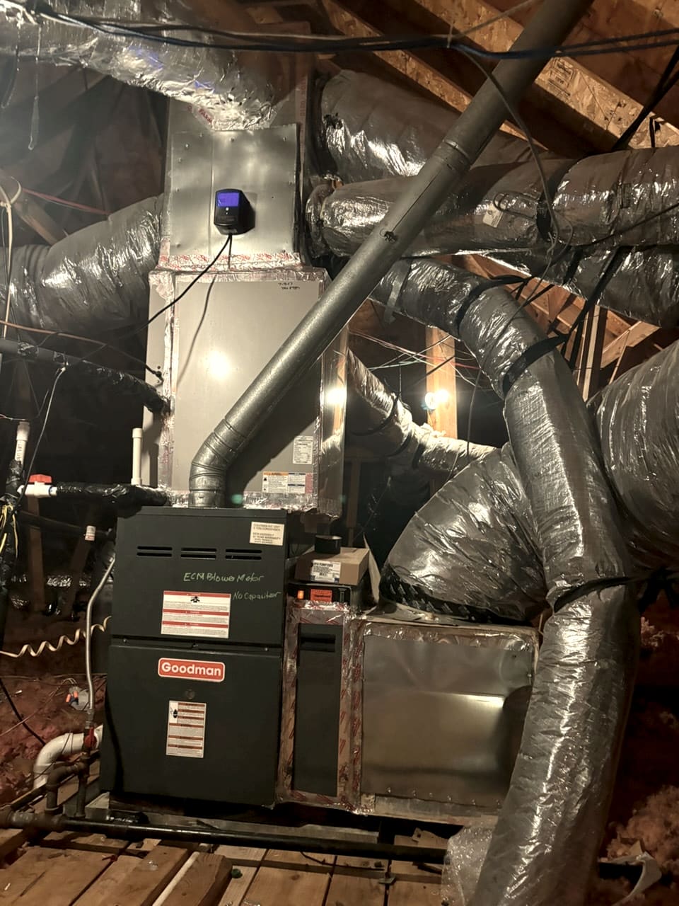 A Goodman furnace in an attic with flexible duct running off it.