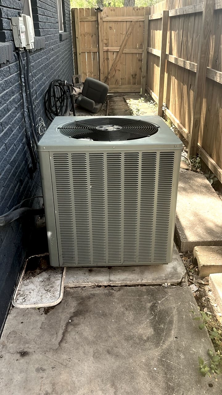 A condenser on its pad in a fenced side yard.