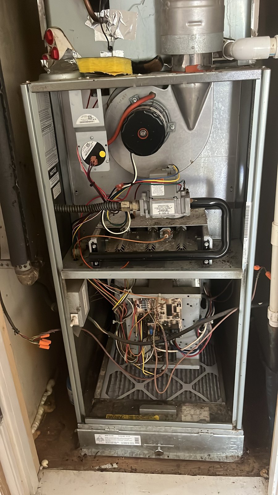 An old furnace in a hallway closet with its panels off, wiring and burners showing.